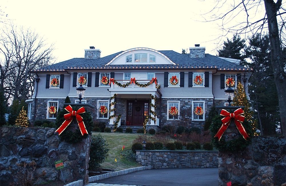 Large stone house decorated with Christmas wreaths, garlands, and red bows at dusk