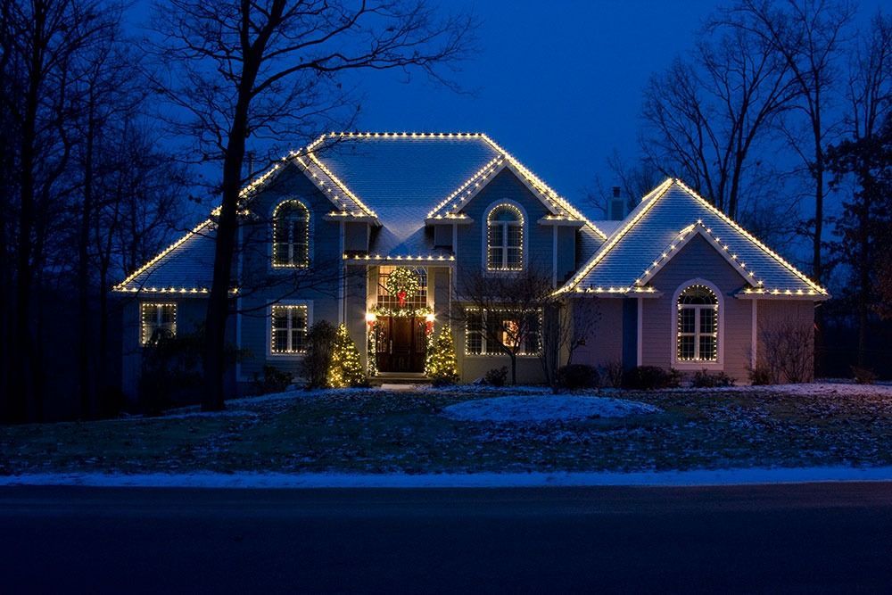House outlined with white holiday lights at night, glowing warmly against a dark blue winter sky