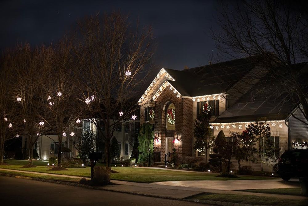 A suburban house at night decorated with warm Christmas lights and lit trees along the street.