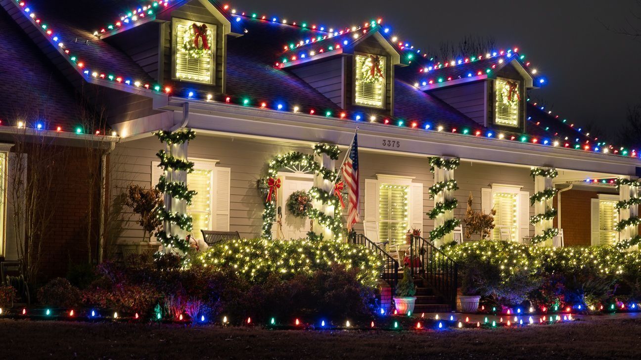 House decorated with colorful Christmas lights at night, with glowing windows and lit shrubs in front
