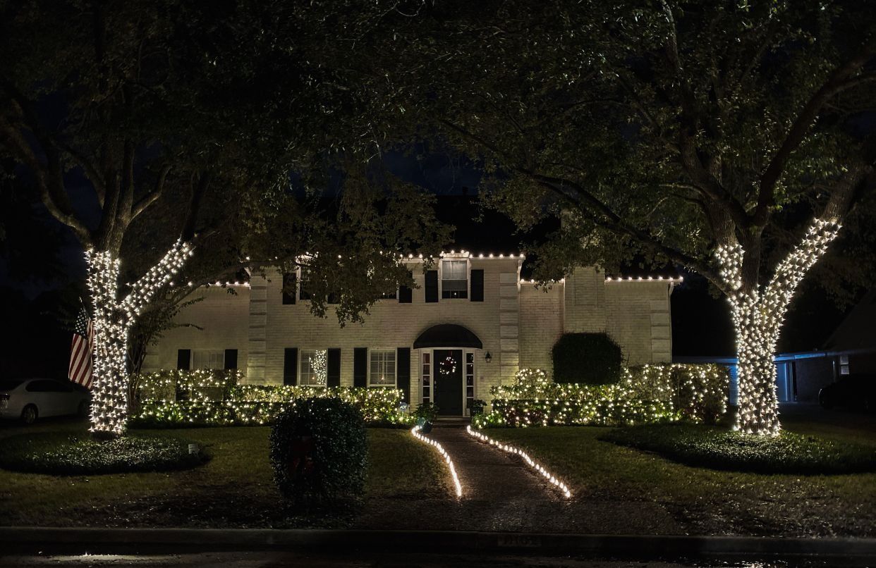 A house at night with trees wrapped in white lights and a lit walkway leading to the front door