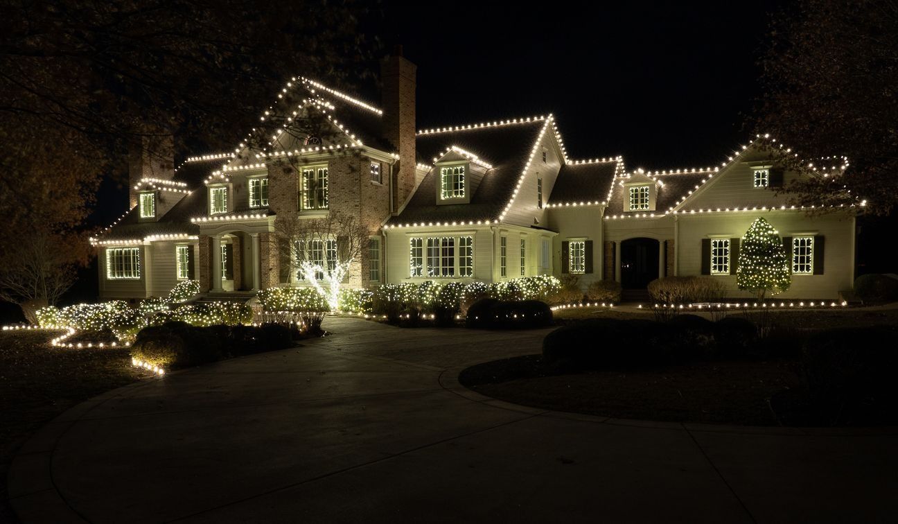 Large house at night outlined with warm white Christmas lights across the roof and windows.