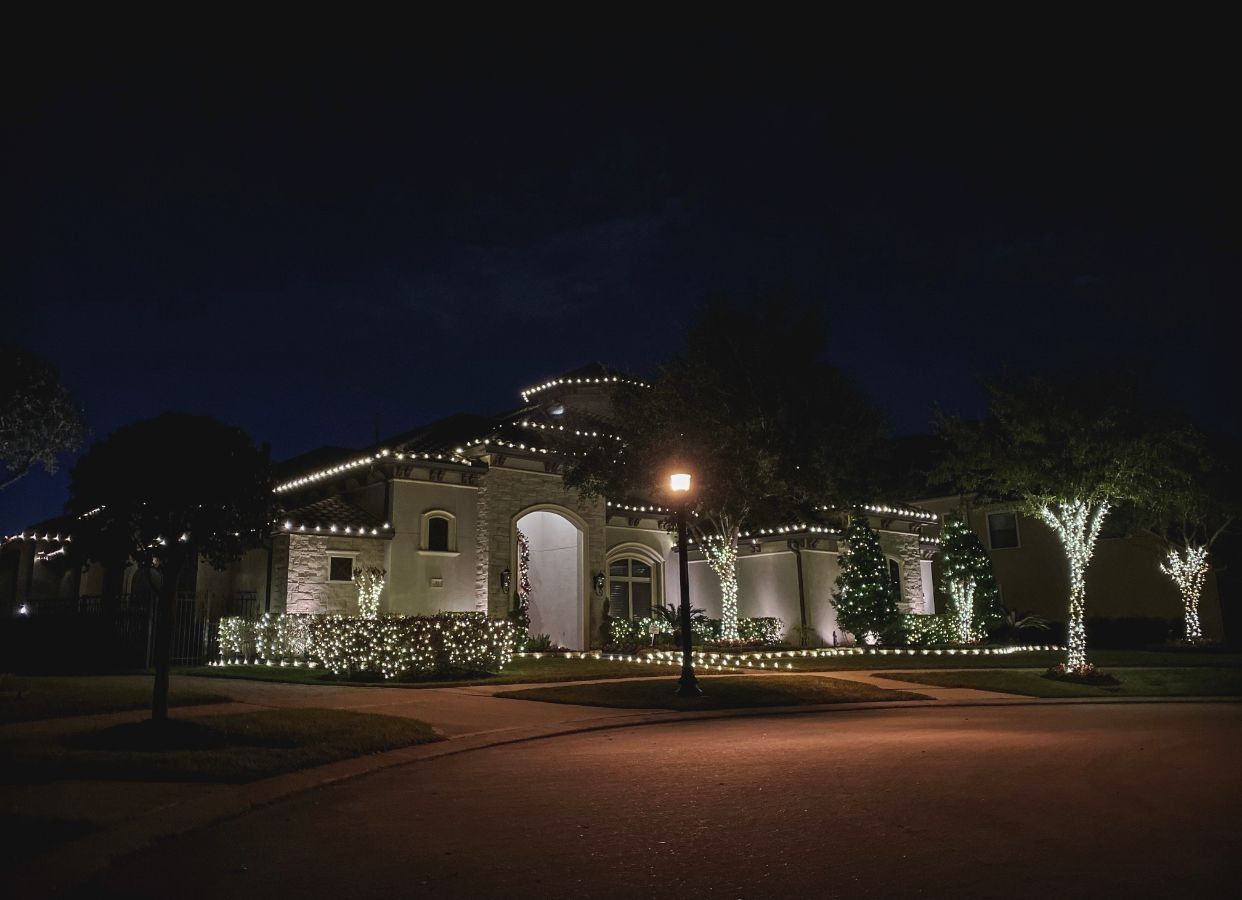 Nighttime view of a lit Mediterranean-style house with arched entry and palm trees lining the driveway