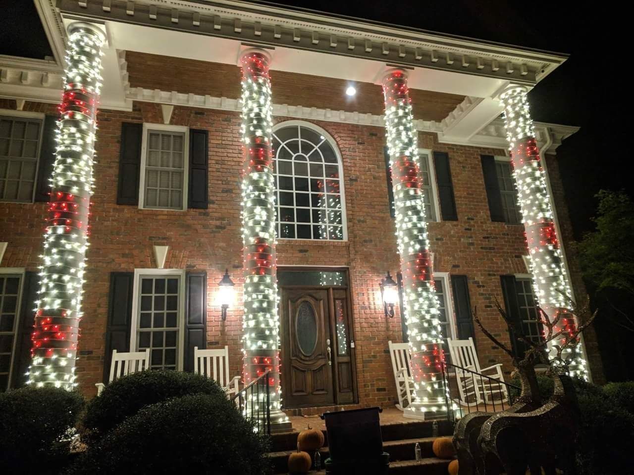 Brick house decorated with white and red Christmas lights on the front columns at night