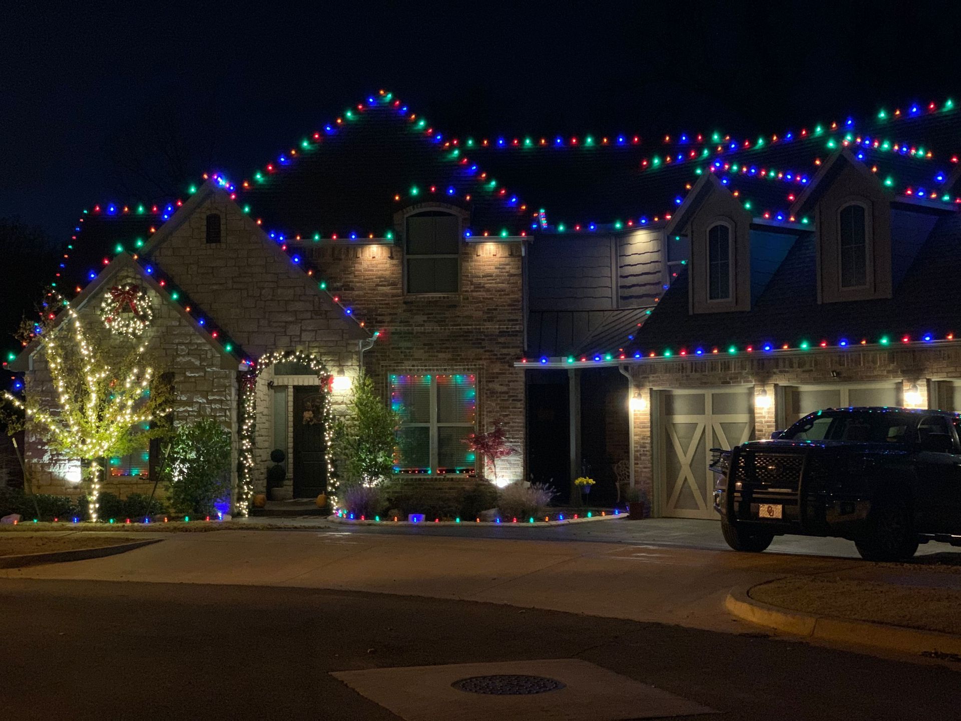 House decorated with colorful Christmas lights at night, with a parked SUV in the driveway