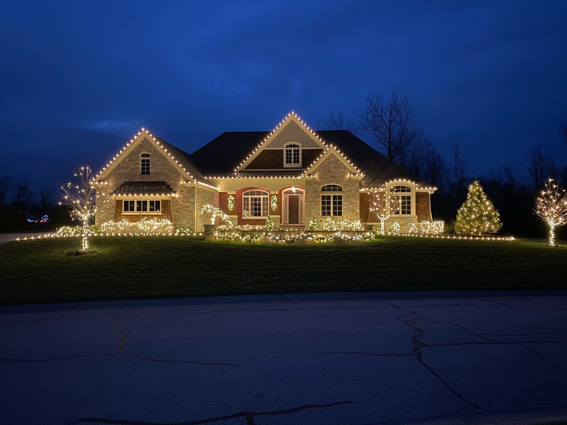 House outlined with warm white holiday lights at night, set against a dark blue sky.
