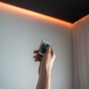 Hand holding a remote pointed at a ceiling with warm orange LED strip lighting