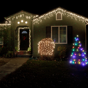 House decorated with white Christmas lights and a multicolored lit tree in the front yard at night