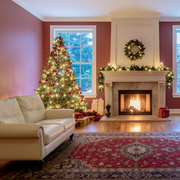 Cozy living room with a decorated Christmas tree, lit fireplace, wreath, and red patterned rug.