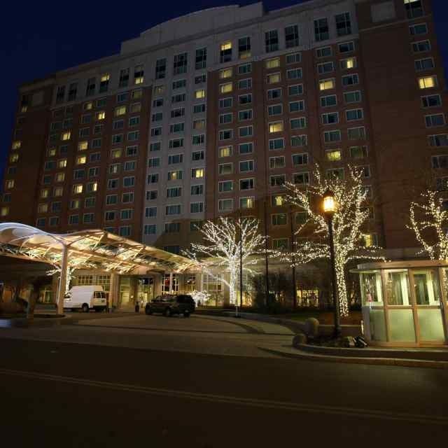 Illuminated apartment building at night with lit trees, a covered entrance, and parked cars