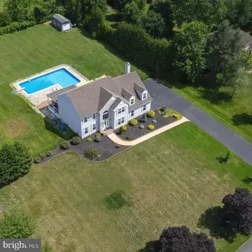 Aerial view of a white house with a backyard pool, driveway, and large green lawn.