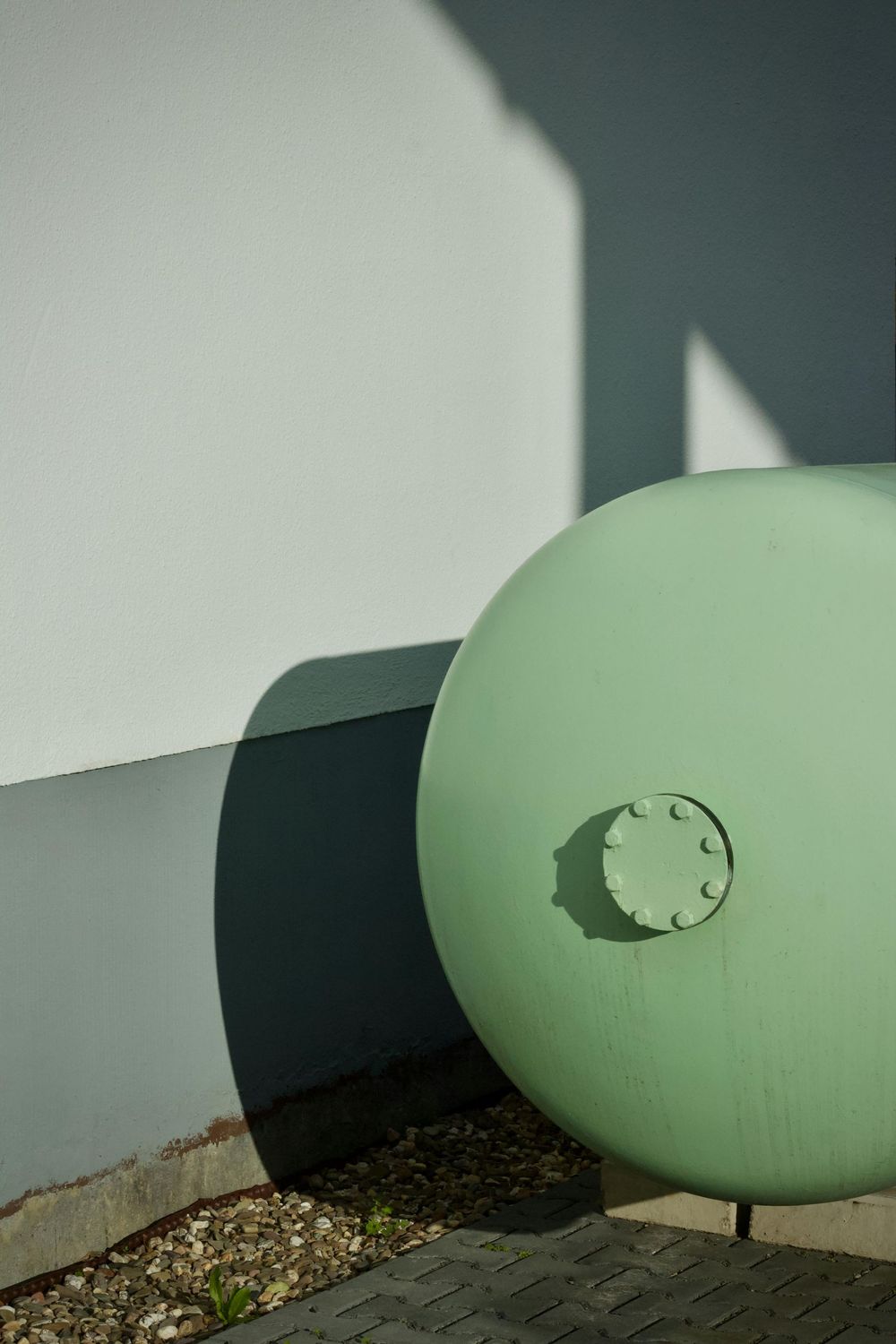 Large pale green sphere sculpture beside a white wall in an outdoor setting