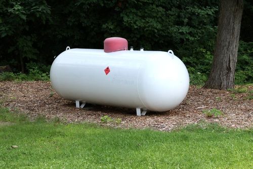 White propane tank on stands in a grassy yard with trees behind it