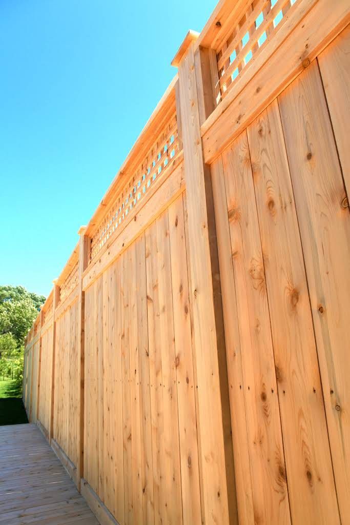 A low-angle view of a new, light-colored wooden fence with a lattice top against a bright blue sky.