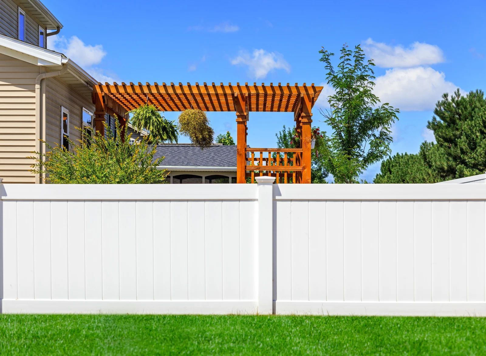 White vinyl fence in front of a house, with a wooden pergola visible above.