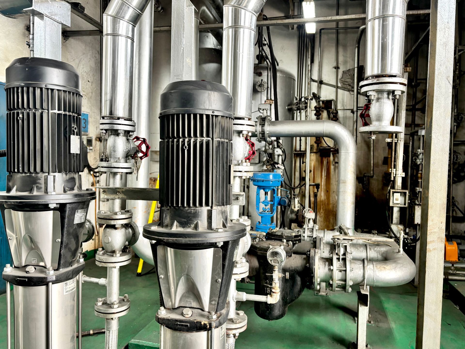 Stainless steel piping with dual vertical pump motors on a green floor.
