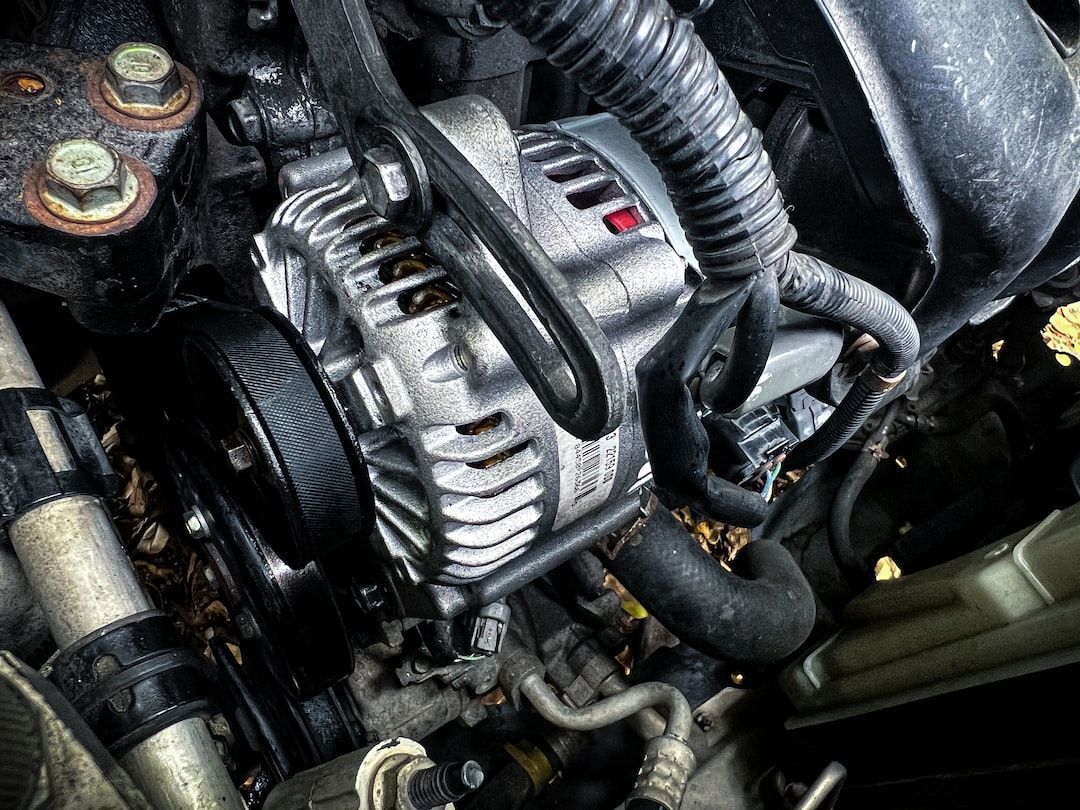 Close-up view of a car alternator within a cluttered engine compartment.