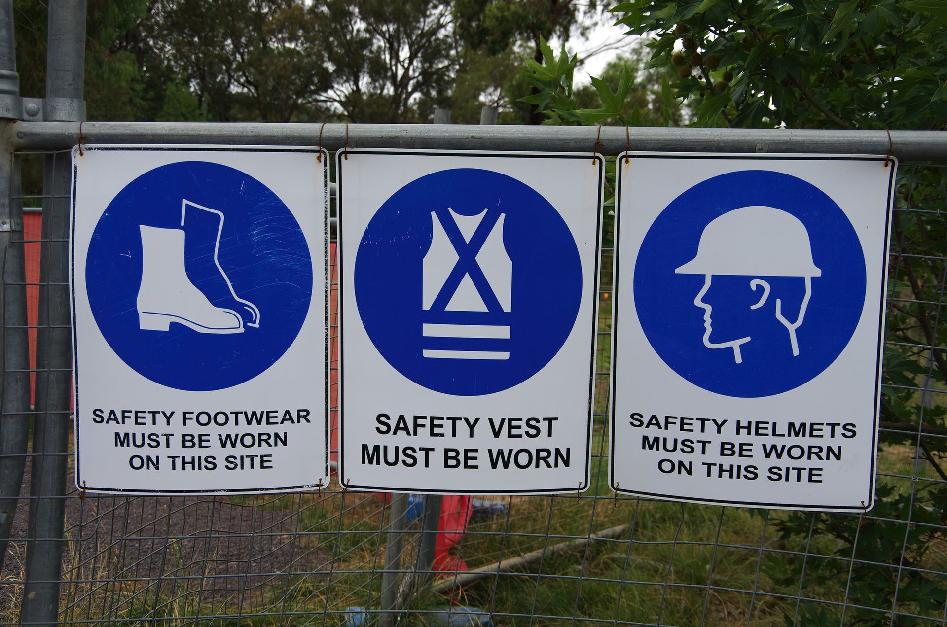 Three blue and white safety signs on a fence one of which says safety footwear must be worn on this site