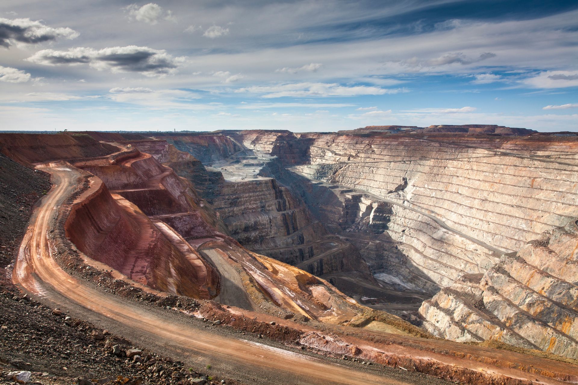 An aerial view of a large open pit mine with a dirt road going through it.