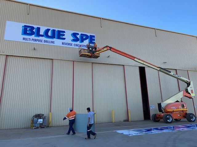 Two men are carrying a piece of wood in front of a building that says blue spe