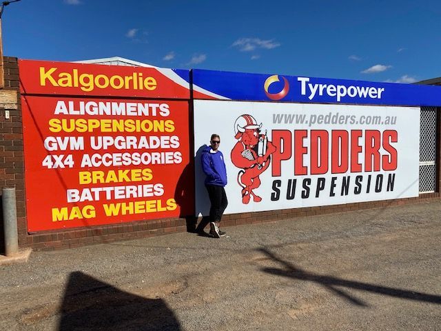 A man is standing in front of a sign for pedders suspension