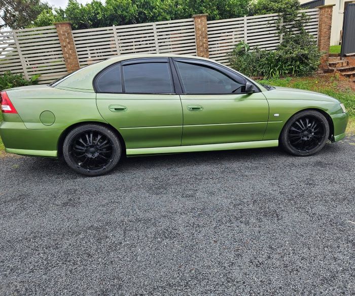 A Green Car is Parked in a Gravel Lot in Front of a Fence — PJ Tinting In Bonny Hills, NSW