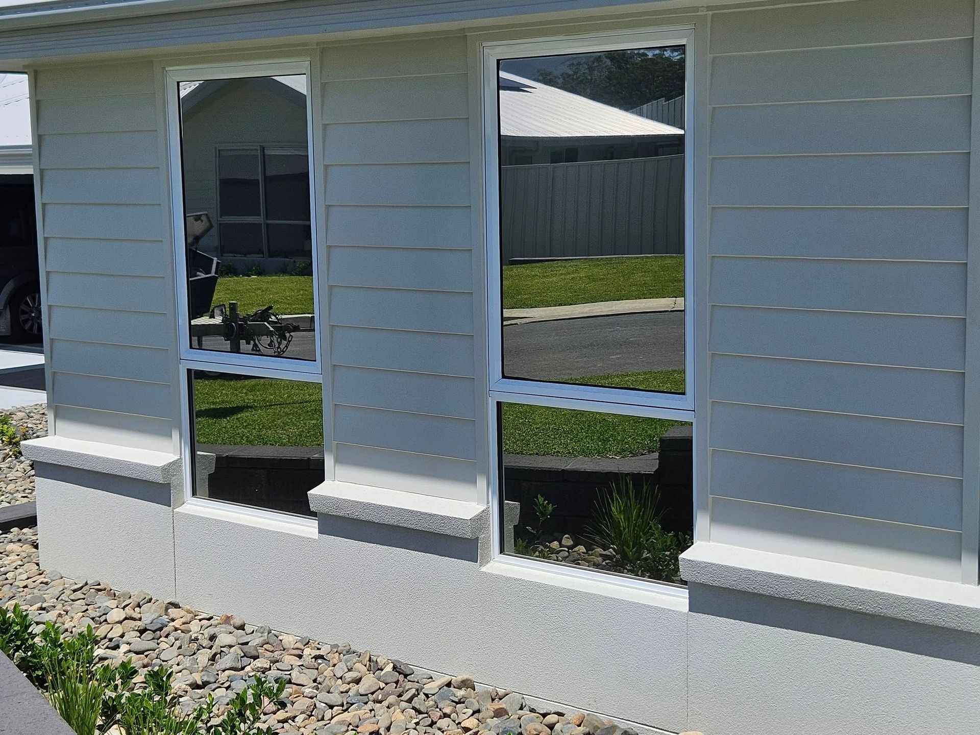 Three rectangular windows with reflective tint on a white house exterior, reflecting the outdoor environment.