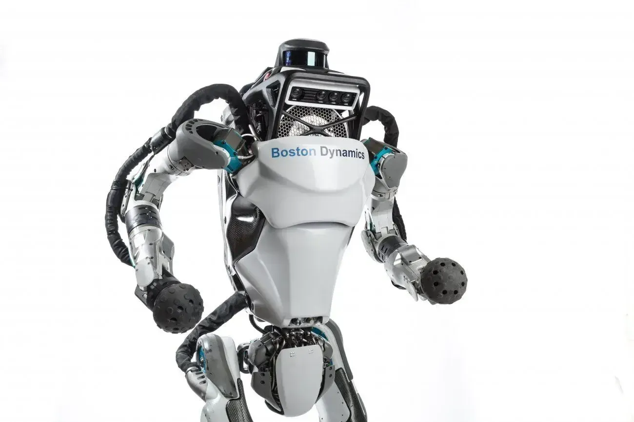 A bipedal robot, Atlas, by Boston Dynamics, standing with arms bent, facing forward.