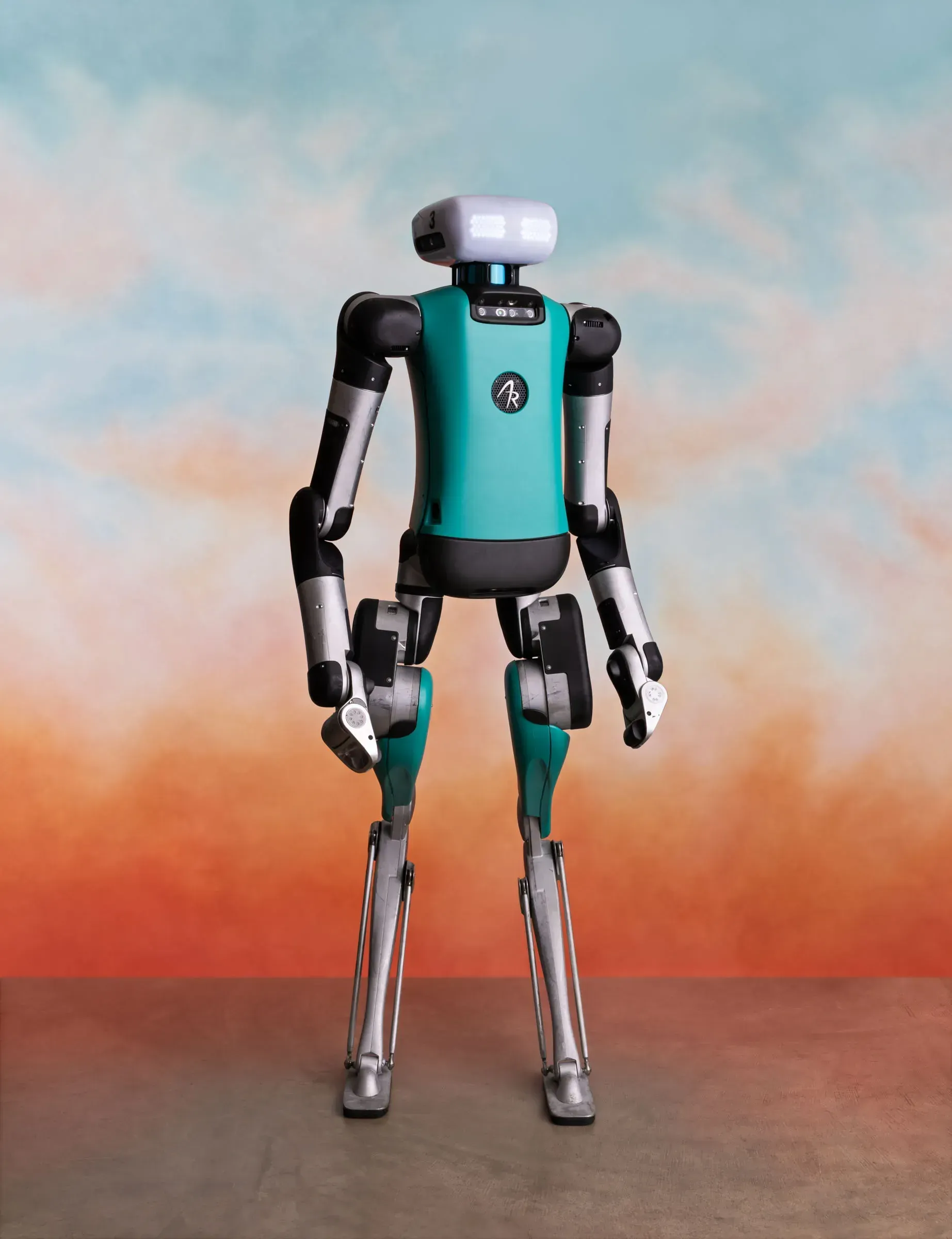 Bipedal robot with teal torso and silver limbs, standing on a brown surface against a cloudy orange and blue backdrop.