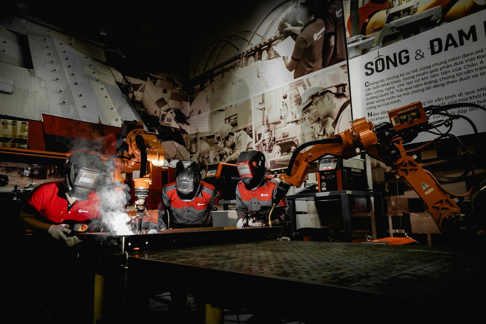 Workers welding metal with robots in a dark industrial space. Sparks fly.