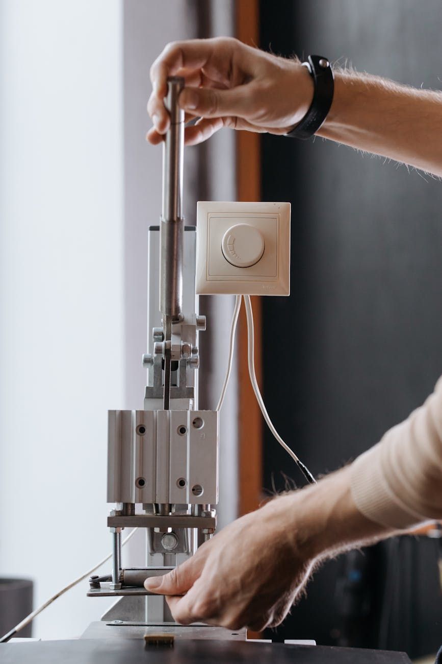 Person operating a small, mechanical device, possibly for testing. The device is silver with a white button nearby.