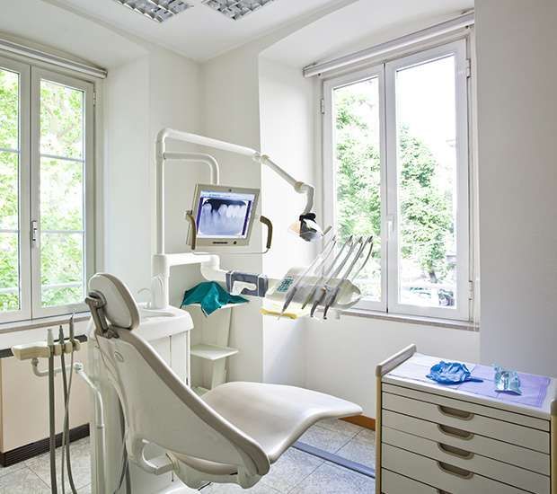 Dentist using blue gloves and metal tools to examine a patient’s open mouth