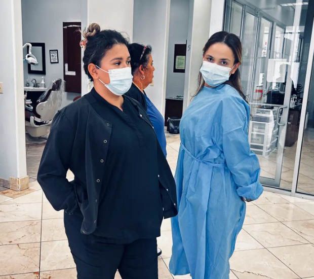 Two masked people standing in a hospital lobby, one in black and one in blue scrubs