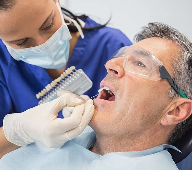 Dentist examining smiling patient in a dental chair with mirror and blue gloves