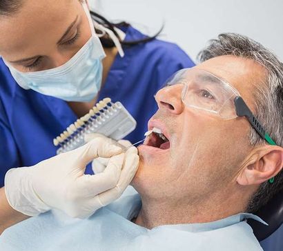 Dentist examining smiling patient in a dental chair with mirror and blue gloves