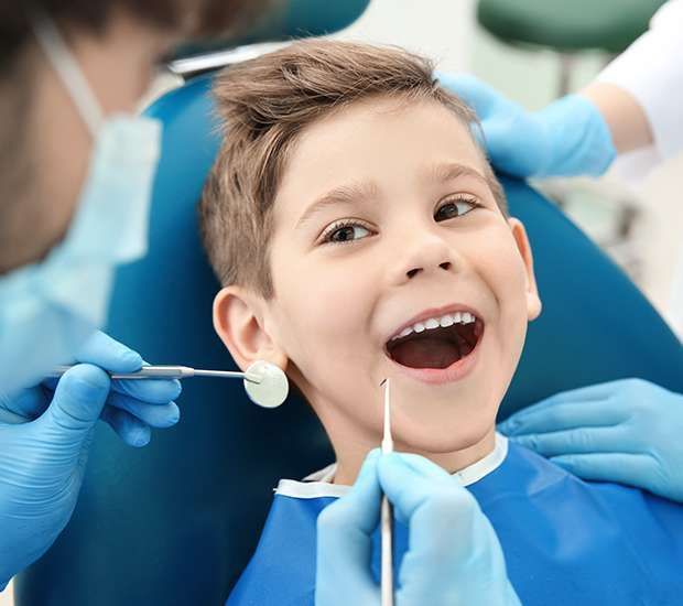 Dentist examining a child’s teeth in a blue dental chair, with gloved hands and dental mirror.