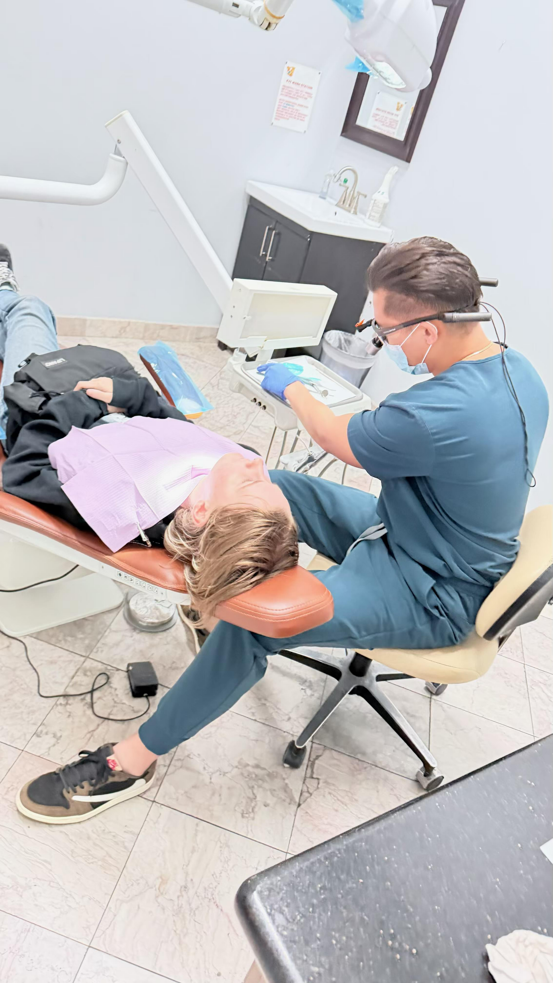 Dental procedure in progress, with a patient reclined in a chair while a dentist works nearby.