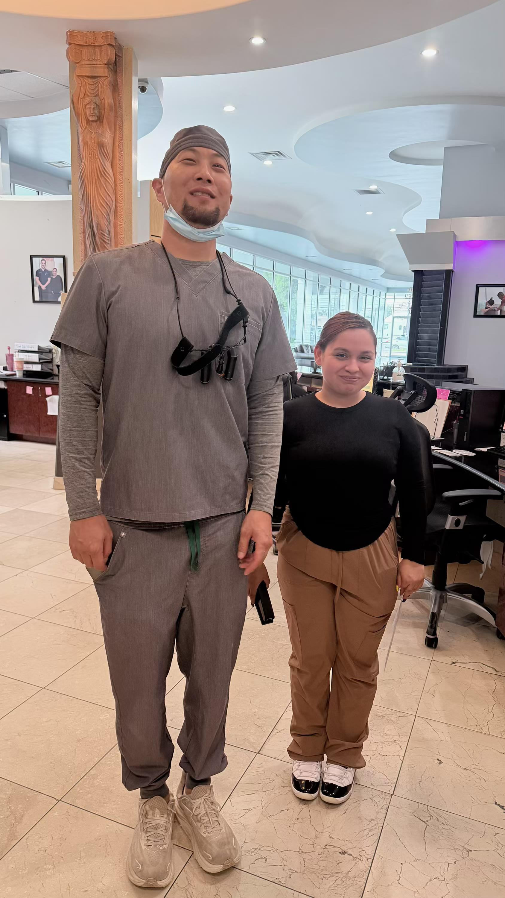 Two people standing in a bright salon, one tall and one shorter, both facing the camera.