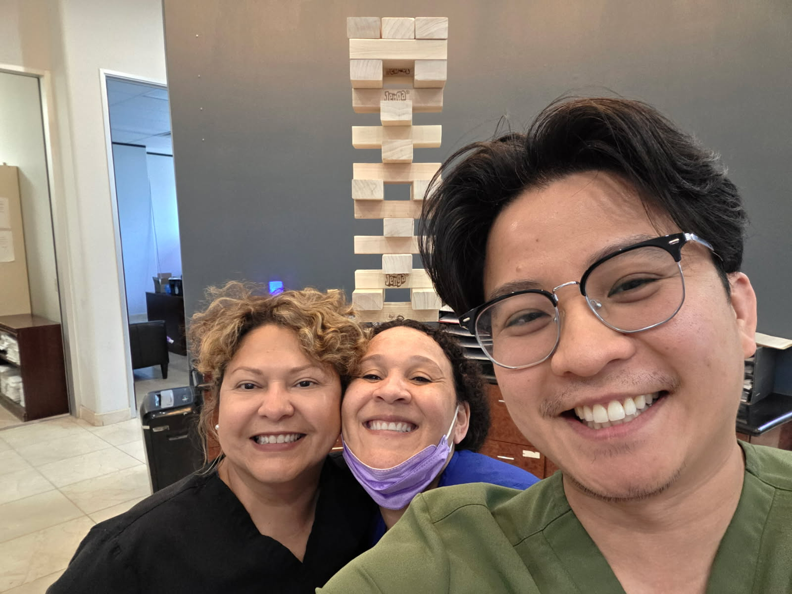 Three smiling people posing indoors in front of a tall block stack.