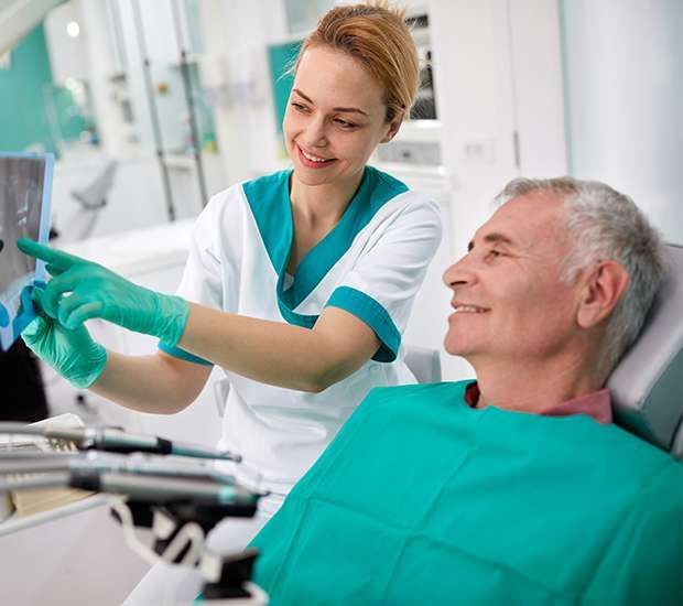 Man holding dentures in one hand and covering his mouth with the other against a purple background