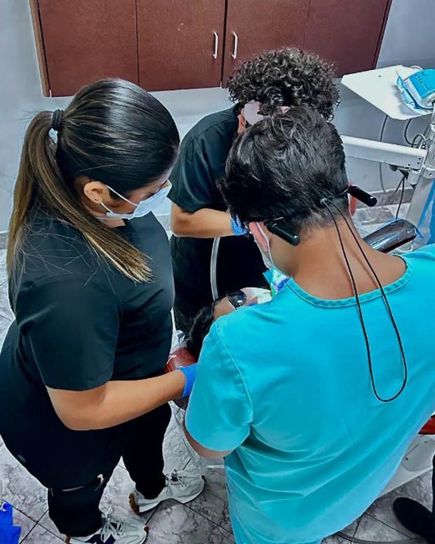 Three people in masks look down at a device together in a room with cabinets.