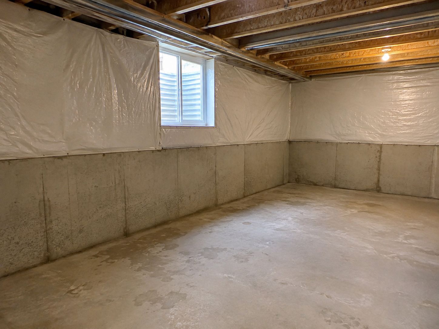 Unfinished basement with concrete walls, exposed joists, white insulation, and a small window.