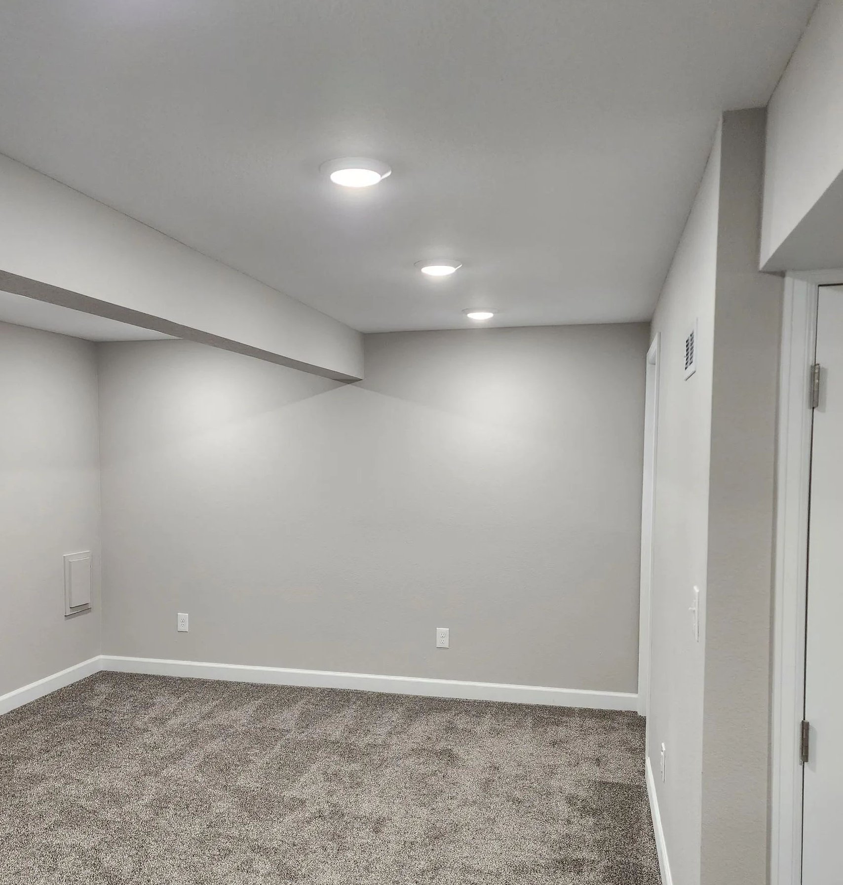 Empty carpeted room with gray walls, recessed lights, and a closet opening on the left.