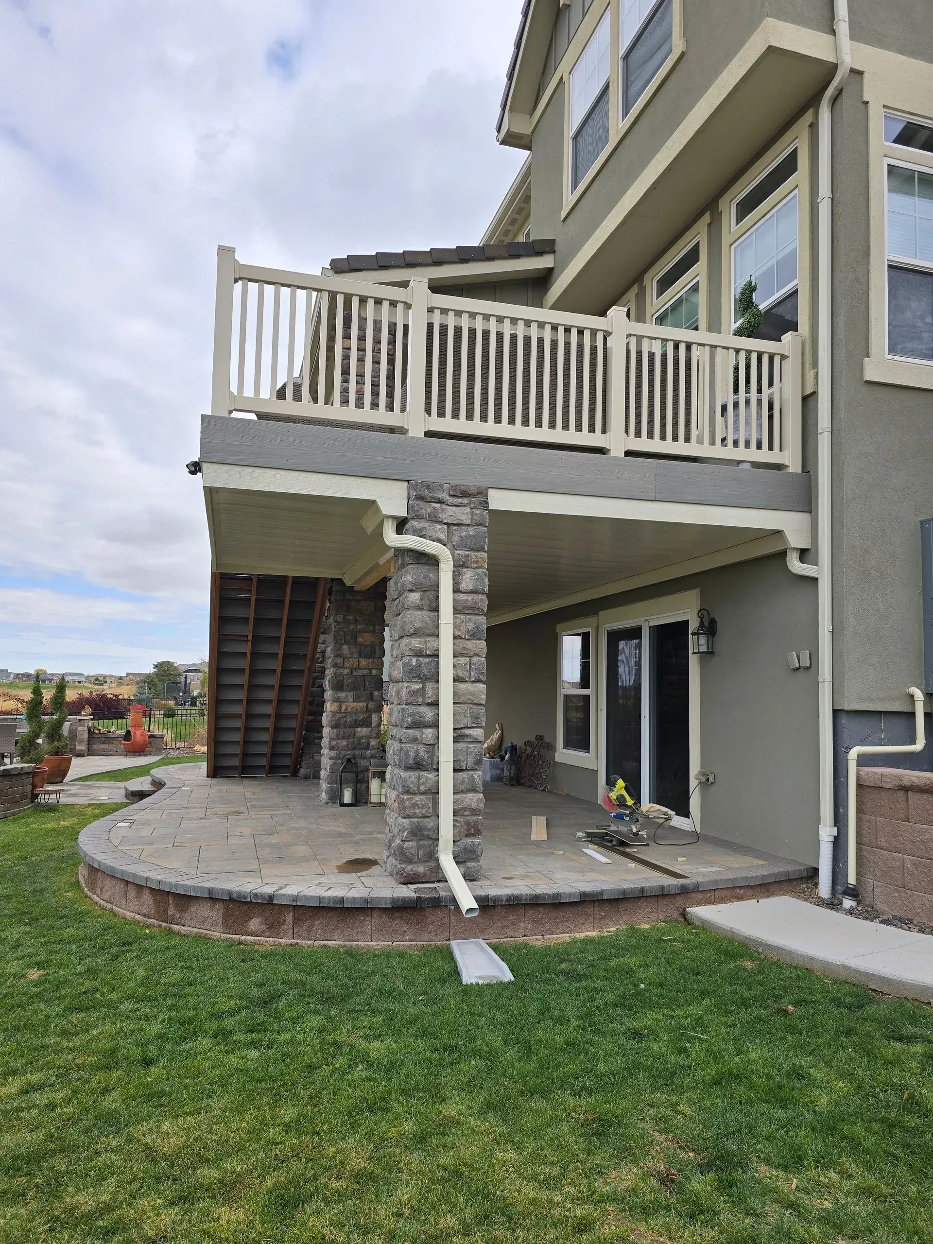 Two-story house patio with stone columns, white balcony railing, and green lawn.
