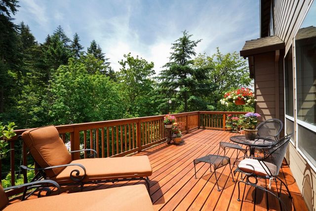 Sunlit wooden deck with lounge chairs, table, and forest view beside a house
