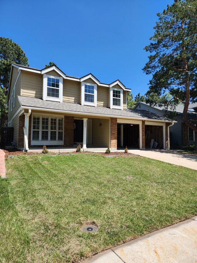 Two-story suburban house with stone facade, front lawn, and blue sky.