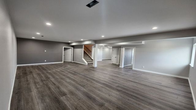 Empty finished basement with gray walls, carpeted floor, recessed lights, and stairway.