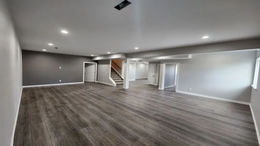 Empty finished basement room with gray walls, carpet, recessed lights, and a staircase to the left.