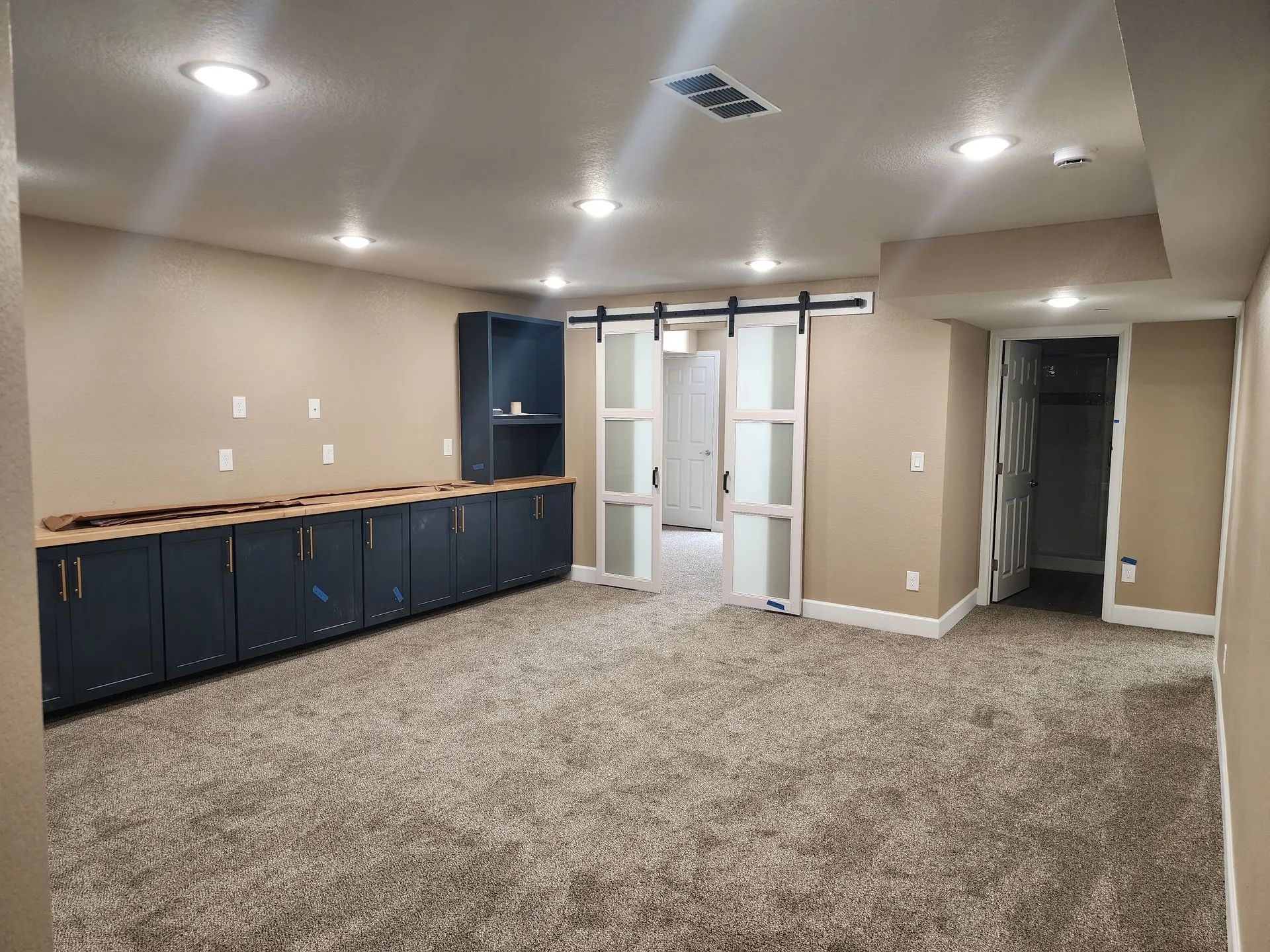 Empty carpeted room with beige walls, recessed lights, blue cabinets, and a central doorway to a closet area