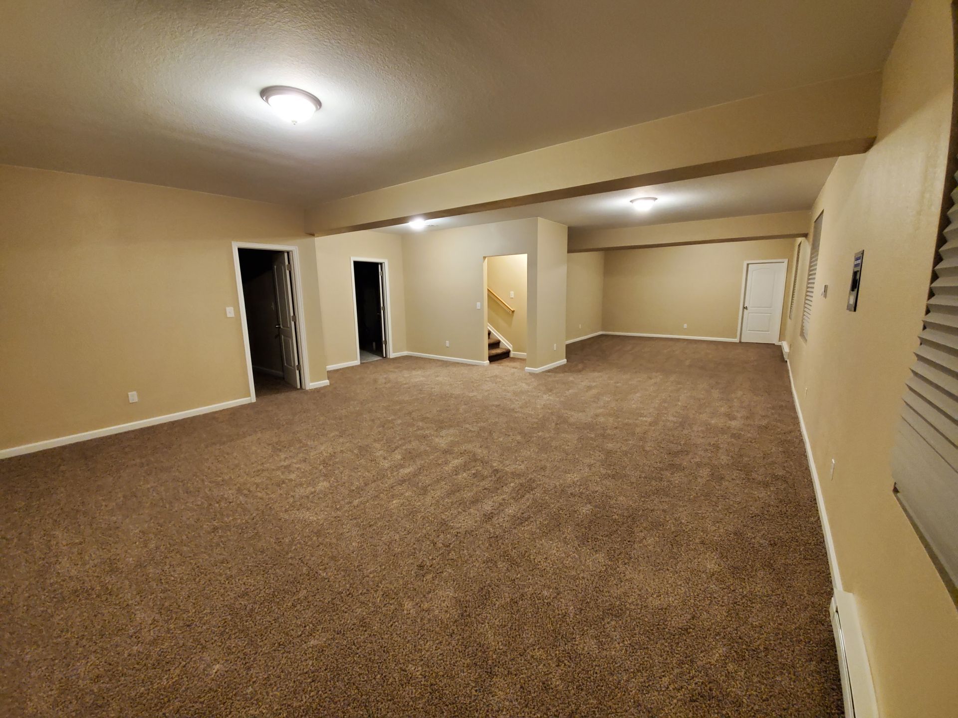 Empty beige carpeted living room with recessed ceiling light and open doorway to stairs in back